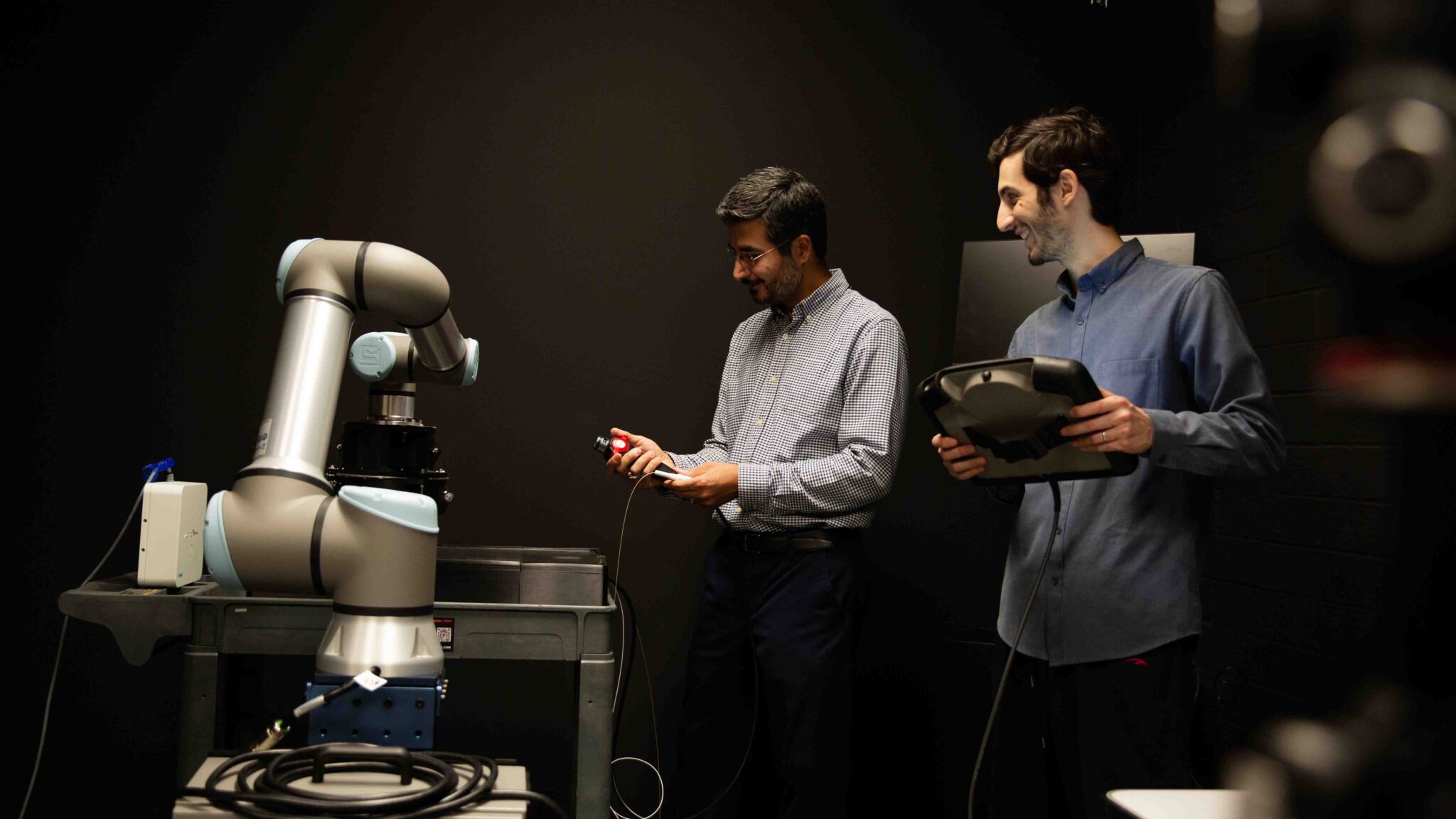 Two people stand in front of lab equipment in front of a dark background.